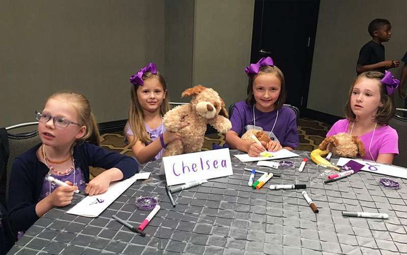 Four young girls wearing purple and holding stuffed PanCAN bears, color signs for National Pancreatic Cancer Advocacy Day
