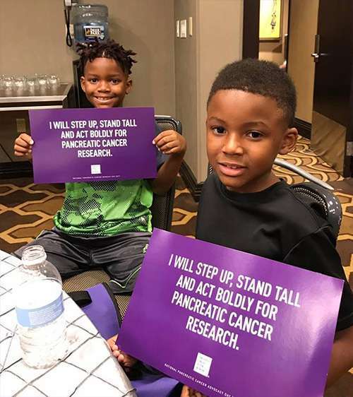 Two young boys smile while holding signs saying they will step up, stand tall and act boldly for pancreatic cancer research