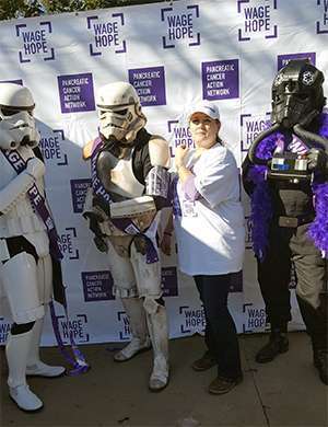 Pancreatic cancer survivor stands with people dressed in white Stormtroopers armor at fundraiser walk