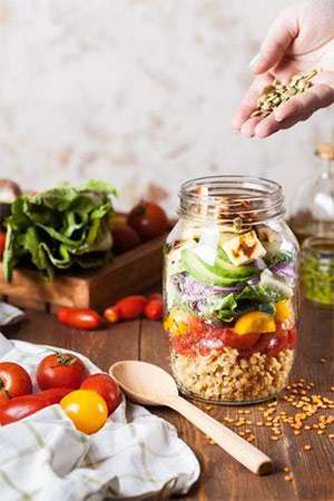 A mason jar filled with ingredients to make a salad, including fresh grains and produce.