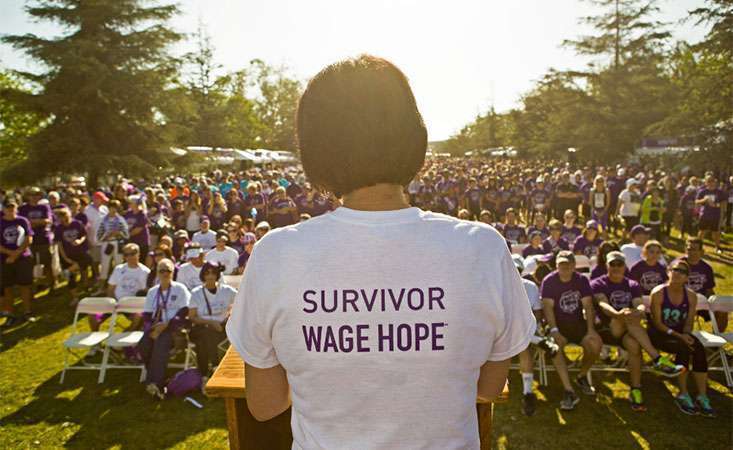 A woman speaks for the pancreatic cancer cause in a shirt that reads “Survivor: Demand Better”
