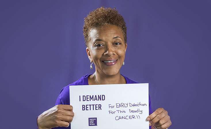 Volunteer holds a sign saying why she Demands Better for pancreatic cancer patients.