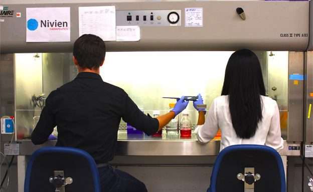 Co-founders of Nivien Therapeutics share a pipette in lab to test a new pancreatic cancer drug
