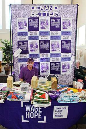 Pancreatic cancer survivor at craft show with quilt handmade from PurpleStride t-shirts