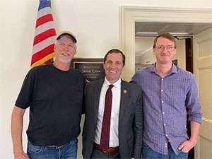 Husband and son of pancreatic cancer patient smile with Congressman Crow in his D.C. office.