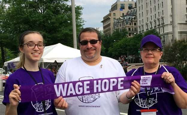 Pancreatic cancer survivor holds “Wage Hope” banner with his wife and daughter at PurpleStride