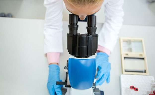 A pancreatic cancer researcher examines cancer cells under a microscope