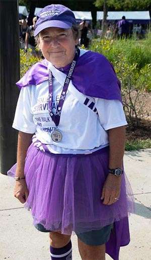 PanCAN volunteer at Louisville cancer walk wearing purple cape and top fundraiser medal