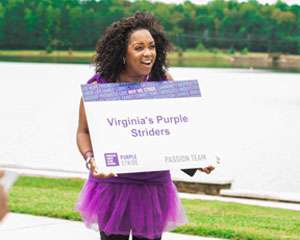 Volunteer decked out in purple holding “Virginia’s Purple Striders” sign 