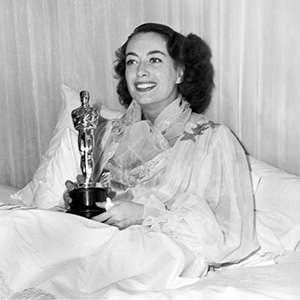 Black and white photo of Joan Crawford accepting her Oscar in bed.