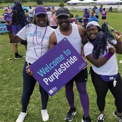 Three PurpleStride attendees holding up a sign saying Welcome to PurpleStride.