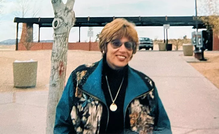 Woman with short reddish hair and sunglasses smiling outside.