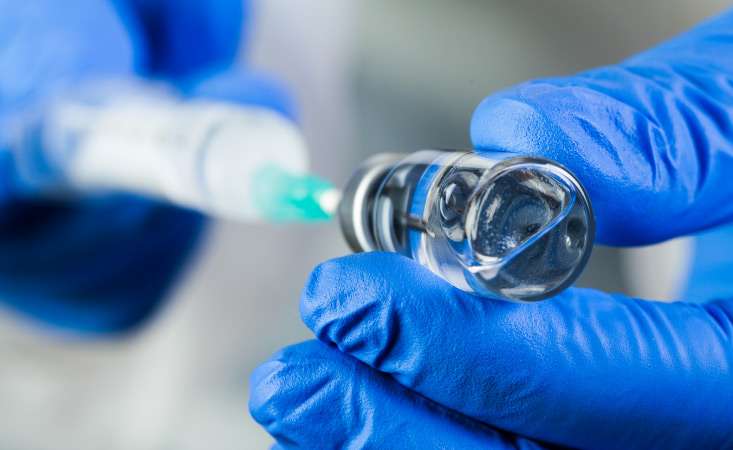 closeup of hands wearing blue rubber gloves holding a vial and syringe
