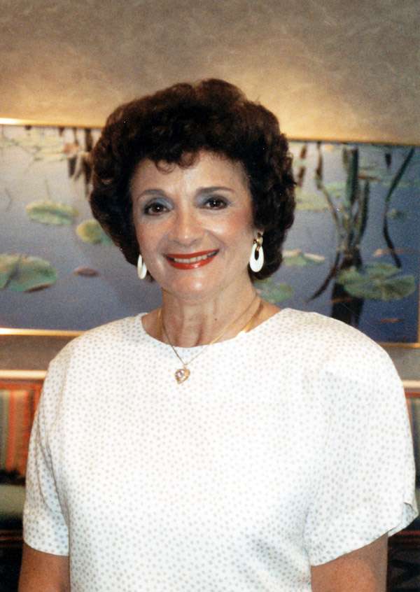 A picture of Estelle Rose, alone, in a white blouse, smiling at the camera.