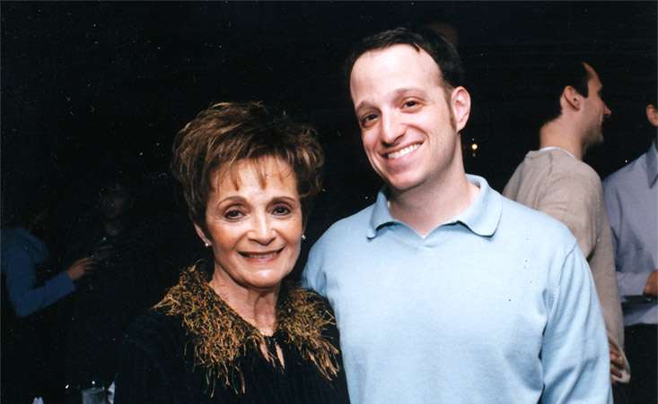 Mother (left) and son (right) standing together smiling, posing for a picture.