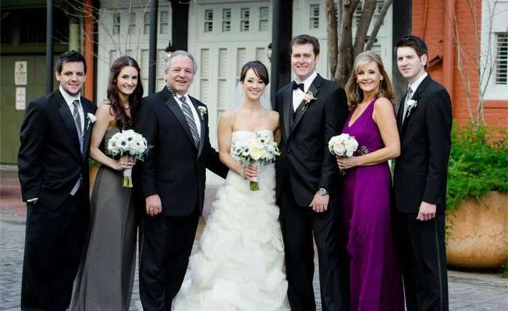 Family of four men and three women, including the bride in her dress, pose for a wedding photo.