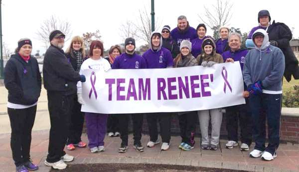 Group photo taken outside of 16 people who are wearing purple and holding a sign that says Team Renee.