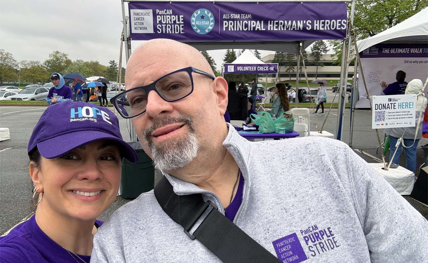 A selfie of a man and woman standing in front of an event tent at PanCAN PurpleStride 2025.