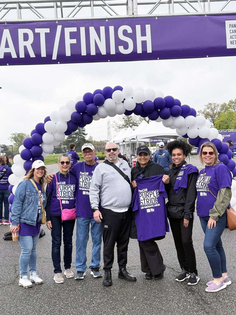 A group of seven people standing in front of a balloon arch at PanCAN PurpleStride 2025.
