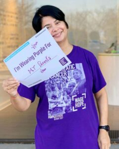 Monica, wearing purple, holds a sign that says “I’m wearing purple for my parents.”
